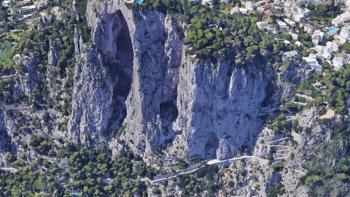 Vista aerea di un'imponente parete rocciosa a sbalzo con vegetazione e strade sottostanti, ambito di applicazione della soluzione Axatel Angel Rock.